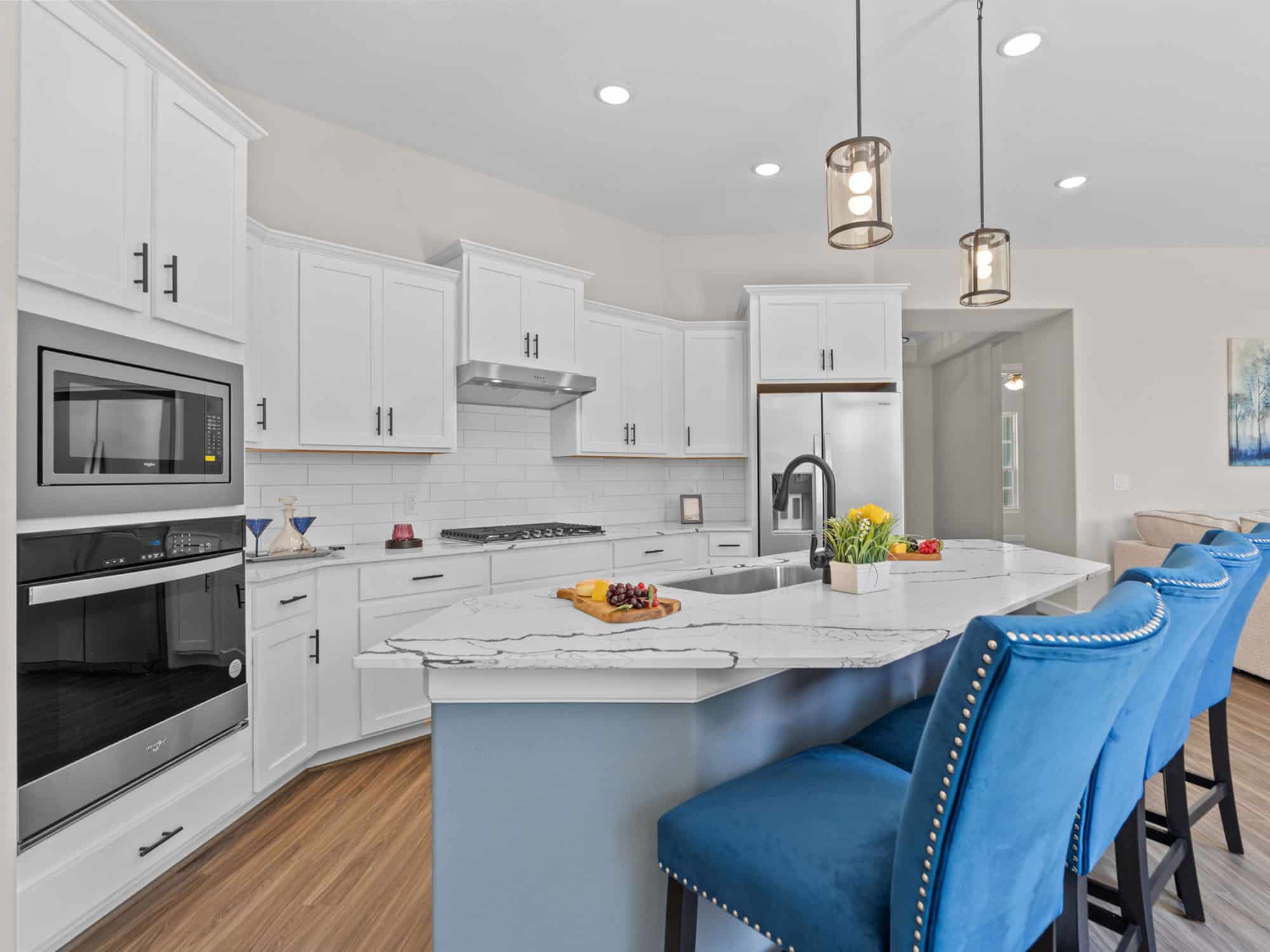 Portico kitchen with quartz island, blue bar stools, and wall ovens at 1306 Hidden Oaks Dr
